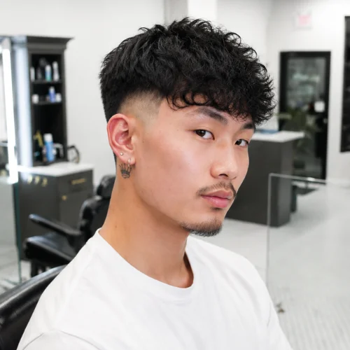 Asian burst fade haircut with textured curly hair in a modern barbershop